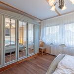 Schlafzimmer mit Holzboden, Kleiderschrank mit Spiegeltüren und Fenster mit weißen Vorhängen.