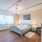 Schlafzimmer mit Bett, Nachttischen, Sessel und Fenster mit Vorhängen.