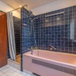 Bad mit Badewanne, Dusche und dunkelblauen Fliesen.