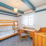 Zimmer mit Doppelstockbett, Schreibtisch und Kinderbett. Holzdecken und Fenster mit Vorhängen.