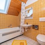 Badezimmer mit Badewanne, Duschvorhang, Waschbecken und WC. Holzdecke und gelbe Fliesen.