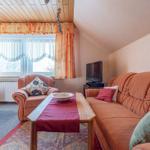 Wohnzimmer mit Sofa, Sessel, Tisch und Fernseher. Fenster mit Vorhängen und Bett im Hintergrund.