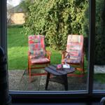 Zwei Stühle mit bunten Kissen und Tisch auf Terrasse mit Grünfläche und Hecke.