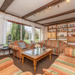 Wohnzimmer mit Sofa, Fernseher und Bücherregal. Blick auf Garten durch Fenster.