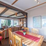 Essbereich mit Holztisch, Stühlen und Karte an der Wand. Wohnbereich mit Sofa und Fernseher.