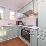 Küche mit hellgrauen Schränken, weißen Fliesen und rotem Terrakottboden.