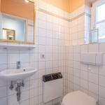 Badezimmer mit Waschbecken, Spiegel, Toilette und Fenster mit Vorhang.