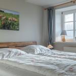 Schlafzimmer mit Bett, Fenster und Wandbild.