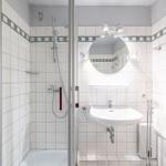 Badezimmer mit Dusche, Waschbecken und Spiegel. Fliesenwand mit Mosaikstreifen.