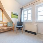 Schlafzimmer mit Holzbank, Stuhl und Fenstern. Wandspiegel und Bild an der Wand.