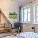 Schlafzimmer mit Dachschrägen, Bett, Bank, Stuhl und Fenster.