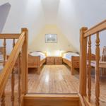 Zwei Einzelbetten mit Nachttischen unter einem Dachfenster. Holzboden und Holzgeländer.