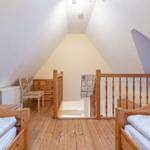 Zimmer mit zwei Betten, Holzboden und Dachschrägen. Holzgeländer und Kleiderschrank sichtbar.