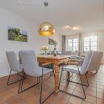 Esszimmer mit Holztisch, grauen Stühlen und goldener Pendelleuchte. Terrakottafußboden und Fenster zur Terrasse.