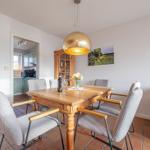 Essbereich mit Holztisch, Stühlen und goldener Deckenleuchte. Küche und Wohnbereich sind sichtbar.