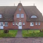 Rotes Backsteingebäude mit Strohdach und weißen Fenstern. Vorgarten mit Weg und Gras.