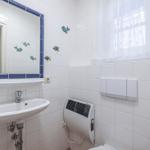 Badezimmer mit Waschbecken, Spiegel und Fenster mit weißen Vorhängen.