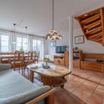 Wohn- und Essbereich mit Holzmöbeln, Terrakottboden und Treppe zur oberen Etage.