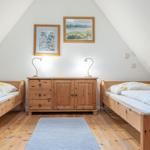 Zwei Betten mit Holzrahmen stehen gegenüber einem Schrank mit Lampen und Bildern an der Wand.