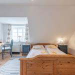 Schlafzimmer mit Holzbett, Schreibtisch und Fenster. Holzfußboden und blaue Nachttische.