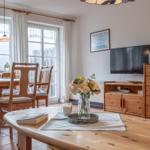 Essbereich mit Holztisch und Stühlen. Fernseher und Holzschrank im Hintergrund.
