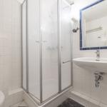 Badezimmer mit Dusche, Waschbecken und Spiegel mit blauem Rahmen.