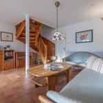 Wohnzimmer mit Holztreppe, Sofa und Esstisch. Terrakottaboden und Holzmöbel.