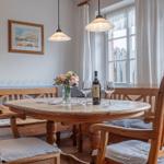 Esszimmer mit Holztisch, Stühlen und Fenster. Auf dem Tisch steht eine Flasche Wein und Blumen.
