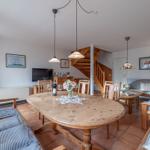 Esszimmer mit Holztisch, Stühlen und Sofa. Treppenhaus im Hintergrund.