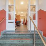 Treppenhaus mit roten Wänden und grauen Stufen führt in einen Flur mit Möbeln.