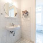 Badezimmer mit Waschbecken, Spiegel und Handtuchhalter. Durchgang zur Toilette.