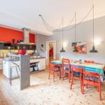 Küche mit Essbereich, rote Wand, farbiger Tisch und Stühle.