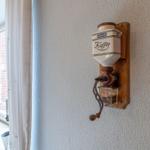 Wandmontierte Kaffeemühle mit Kaffeefass und Handkurbel.