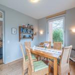 Esszimmer mit Holztisch, Rattanchairs und Fensterblick auf Garten.