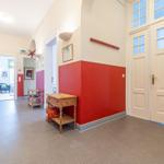 Flur mit rotem Wandabschnitt, Holzmöbel und Türen mit Glasfenstern.