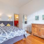 Schlafzimmer mit Bett, Holzschrank und Spiegel. Tür führt in angrenzenden Raum.