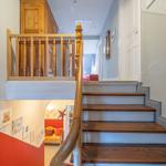 Holzgetreppe mit Geländer führt zur oberen Etage. Unterhalb befindet sich ein Raum mit roter Wand.