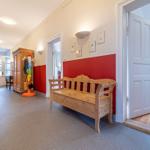 Hallenflur mit Holzbank, roter Wand und Türöffnung zu einem Zimmer.