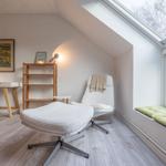 Ein Schlafzimmer mit Dachfenster, Schreibtisch, Stuhl und weißem Sessel mit Fußstütze.