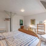 Schlafzimmer mit Bett, Schreibtisch, Stühlen und Regal. Holzbalken an der Decke.