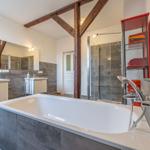 Badezimmer mit Badewanne, Dusche und Waschbecken. Holzbalken und roter Handtuchhalter.