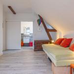 Schlafzimmer mit Dachschrägen, Bett mit orangefarbenen Kissen und Blick in die Badewanne.