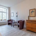 Ein Zimmer mit zwei Sesseln, einem Schrank und einem Fenster mit Blick auf Bäume.