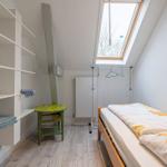 Schlafzimmer mit Dachfenster, Bett, Kleiderständer und Regalwand.