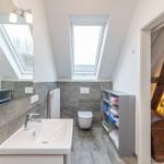 Badezimmer mit Waschbecken, Toilette und Dachfenster. Nebenraum mit Bett und Holzkonstruktion.