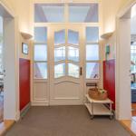 Eingang mit Glasfronttür, roten Wänden und Blick in Wohn- und Essbereich.