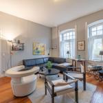 Wohnzimmer mit Sofa, Stühlen, Tisch und Fenstern mit weißen Vorhängen.