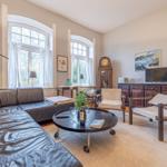 Ein Wohnzimmer mit Ledersofa, zwei Sesseln und zwei großen Fenstern.