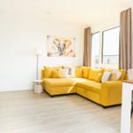 Ein Wohnzimmer mit gelbem Ecksofa, Wandbild und Essbereich.