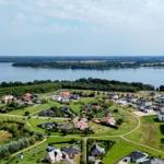Luftbild von Wohnhäusern am See mit grünen Wiesen und Bäumen im Hintergrund.